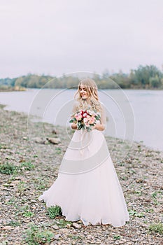 Sensitive full-length photo of the beautiful bride holding the wedding bouquet. Beach location.