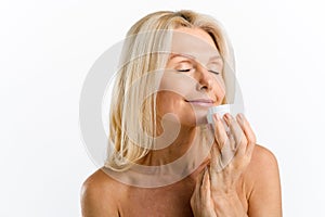 Sensitive middle-aged woman holding jar of moisturiser rich cream in hand