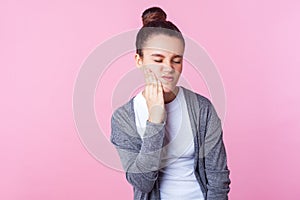 Sensitive teeth. Portrait of unhealthy teenage girl touching chin and frowning from terrible toothache. pink background