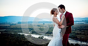Sensitive wedding portrait of the cute newlywed couple. Background of the magnificent landscape during the sunset.