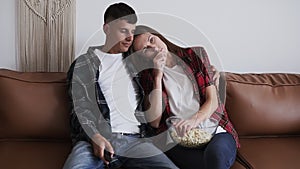 Sensitive woman is watching TV and crying while husband is at home. Couple sitting on brown leather couch, husband