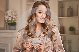 Sensitive young woman delights her morning coffee.