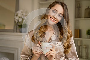 Sensitive young woman delights her morning coffee.