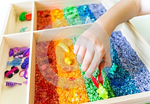 Sensory box with rainbow rice inside. Montessori material baby