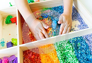 Sensory box with rainbow rice inside. Montessori material baby