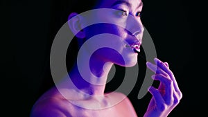 Sensual Asian Woman Applying Lipstick With Brush, Standing Under Bright Neon Light