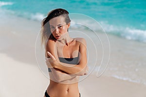 Sensual beautiful girl in black swimsuit resting near ocean on beach