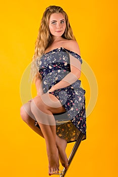 Sensual blond in dress sits on chair on yellow background