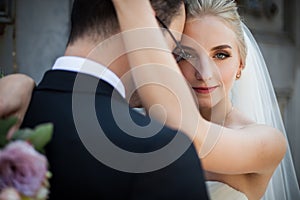 Sensual blonde bride hugging strong groom, face closeup