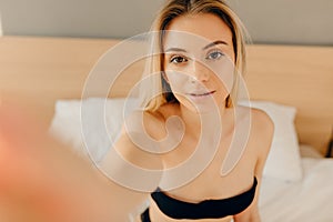 Sensual blonde woman in black underwear looking at camera while lying in bed