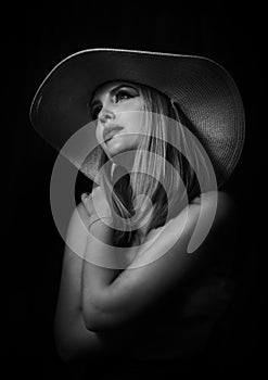 Sensual blonde woman with large hat posing in glamor lighting