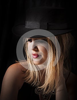 Sensual blonde woman with long hair and black fedora posing in glamor lighting