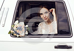 Sensual bride with dark hair in luxurious wedding dress posing in car