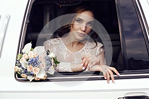 Sensual bride with dark hair in luxurious wedding dress posing in car