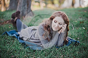 Sensual brunette lady with pout pink lips and white cheeks wearing casual cosy sweater with fur posing sit for on green grass in a