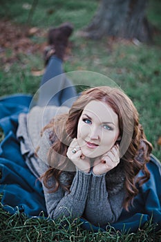 Sensual brunette lady with pout pink lips and white cheeks wearing casual cosy sweater with fur posing sit for on green grass in a