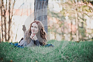 Sensual brunette lady with pout pink lips and white cheeks wearing casual cosy sweater with fur posing sit for on green grass in a