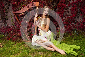 Sensual caucasian female harpist posing with harp against ivy wall outdoor