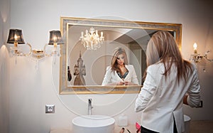 Sensual elegant woman in office outfit looking into a large mirror. Beautiful and blonde young woman wearing jacket