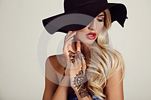 Sensual girl in elegant black hat with mehendi pattern on hands