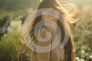 Sensual girl with full lips and fluttering shinning hair at sunset on green meadow. Sensual girl in beige outfit with