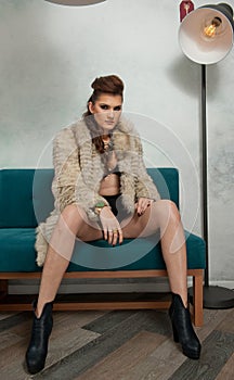 Sensual girl with long legs ,black boots and  fur coat sitting on coach in bar