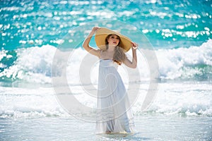 Sensual girl with straw hat enjoying sunbath at beach. Sexy tanned woman enjoying breeze at seaside. Carefree woman