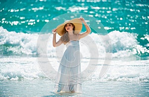 Sensual girl with straw hat enjoying sunbath at beach. Sexy tanned woman enjoying breeze at seaside. Carefree woman