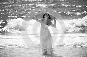 Sensual girl with straw hat enjoying sunbath at beach. Sexy tanned woman enjoying breeze at seaside. Carefree woman