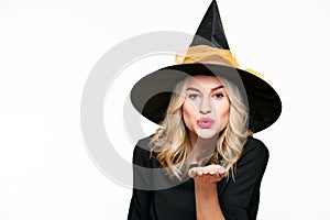 Sensual Halloween Witch Studio Portrait. Attractive young woman dressed in witch halloween costume blowing a kiss towards camera.