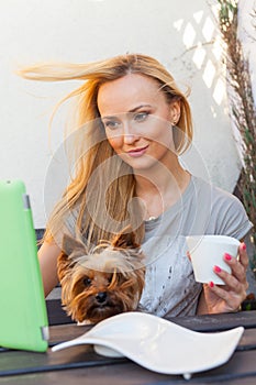 Sensual happy blonde woman sitting on wooden bench. She is using mobile tablet pc. Outdoor photo. She looks relaxed.