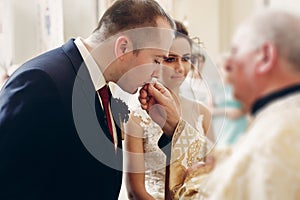 Sensual happy bride kissing wedding ring during wedding ceremony in christian catholic church, priest holding wedding ring in