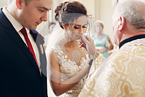 Sensual happy groom kissing wedding ring during wedding ceremony in christian catholic church, priest holding wedding ring in