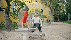 Sensual performers dancing latino choreography in park. Woman spinning on bench.
