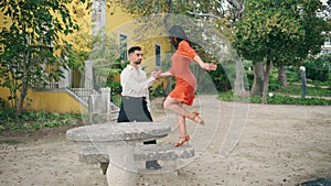 Sensual performers dancing latino choreography in park. Woman spinning on bench.