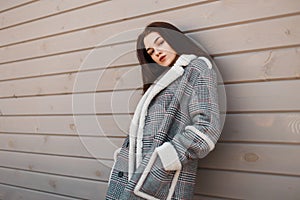 Sensual pretty young brunette woman in a gray luxurious checkered jacket with a white collar is resting standing