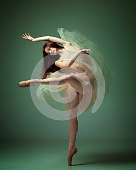 Sensual red haired ballerina wearing tulle dress dancing with emotions over dark green studio background. Weightless