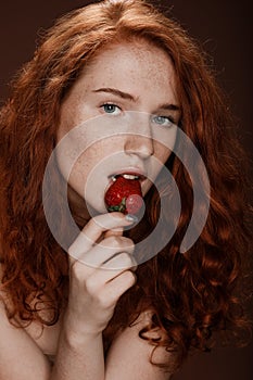 Sensual redhead woman eating fresh strawberry, on brown