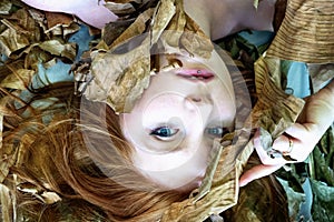 Sensual seductive portrait of a young sexy woman with red hair lying between leaves of a dry decorative banana tree, on the studio