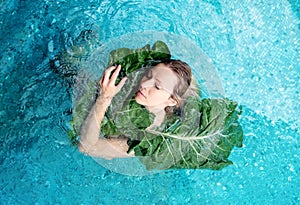 Sensual seductive young woman nestles in the water against a large green plant leaf, in spa wellness pool. skin care concept