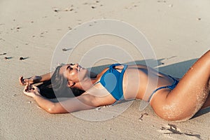 Sensual sexy girl in blue swimsuit lying on white sand at ocean beach