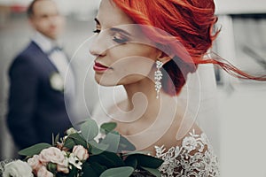 Sensual stylish bride holding modern bouquet and relaxing with windy hair and groom looking at her near retro car. luxury wedding