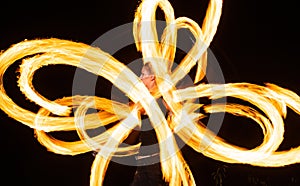 Sensual woman artist perform fiery twirly trails by spinning flaming pois during fire performance in night darkness