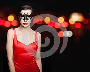 Sensual woman in black carnival mask wearing red silky dress on abstract night glitter bokeh background