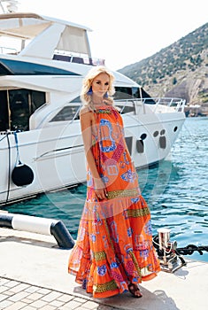 Sensual woman with blond hair in luxurious dress with accessories posing near yacht in dock