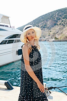 Sensual woman with blond hair in luxurious dress with accessories posing near yacht in dock