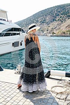 Sensual woman with blond hair in luxurious dress with accessories posing near yacht in dock