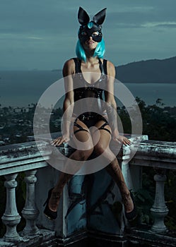 Sensual woman in blue wig with leather belts and rabbit mask