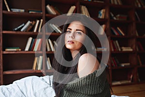 Sensual woman with dark hair in green sweater and jeans sitting on a bed