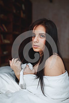 Sensual woman with dark hair sitting on a bed